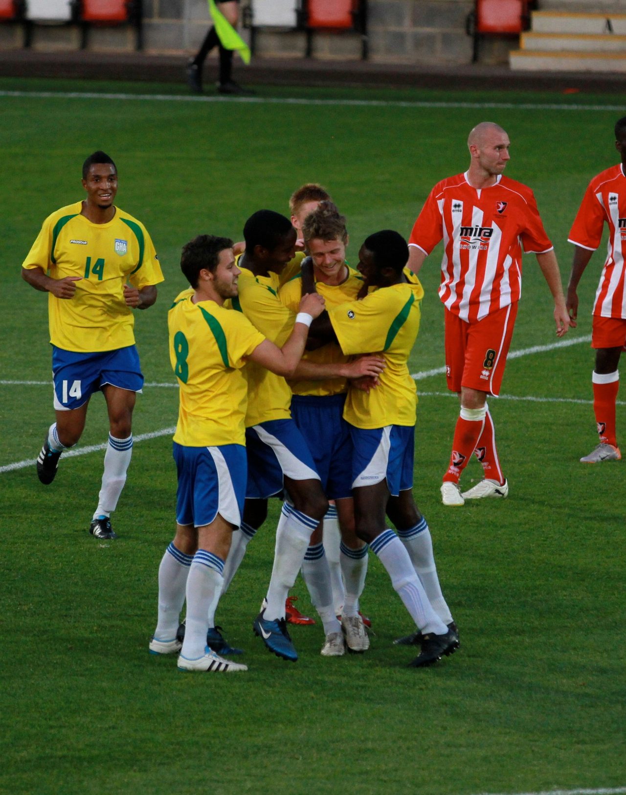 Football players in yellow and red kits standing together on a grass pitch.
